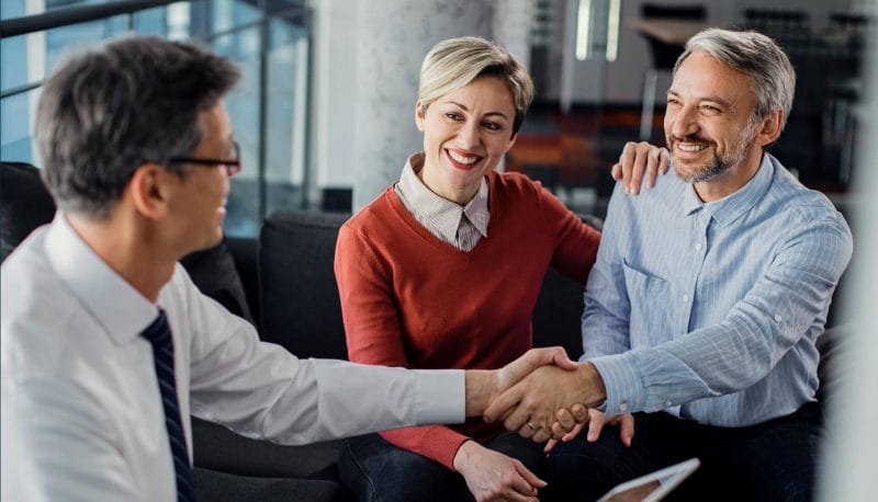 A man shakes hands with another man and woman, symbolizing collaboration and agreement in a professional setting.